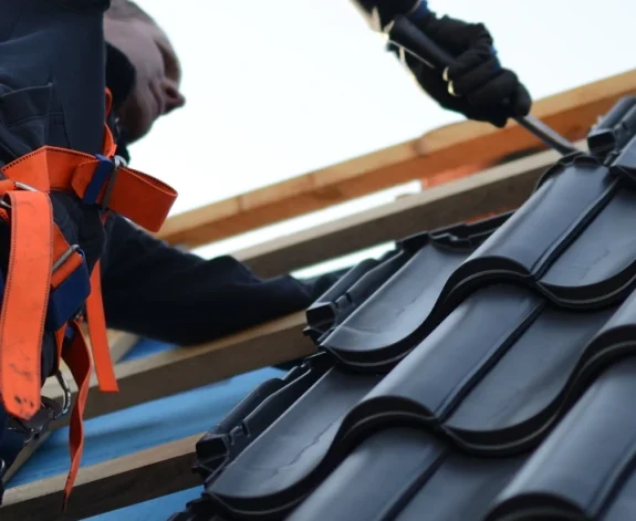 En takläggare lägger noggrant svarta tegelpannor på ett nytt hustak i Borås och Göteborg.